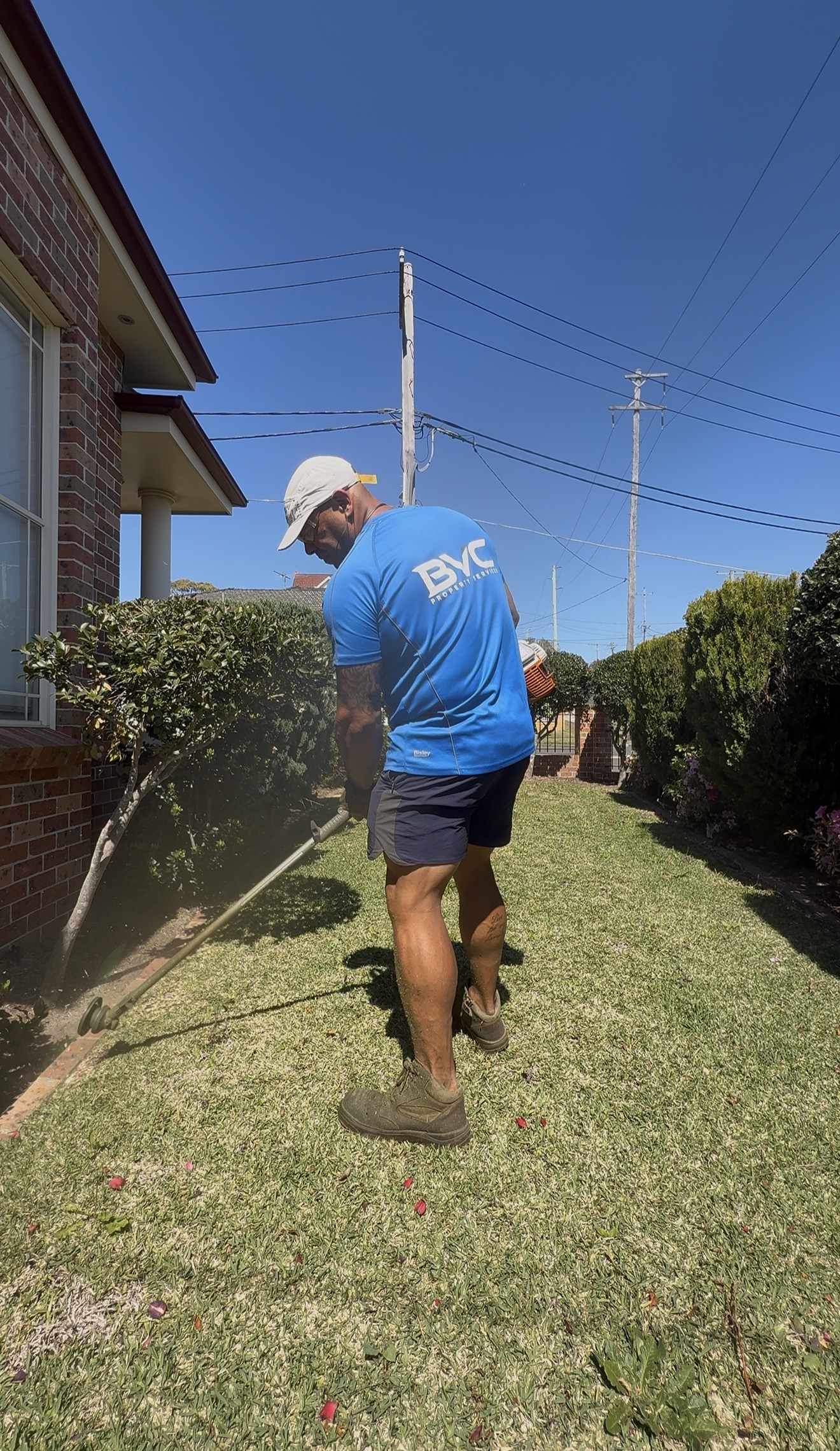 BVC crew member in a blue BVC shirt edging a lawn beside a brick house